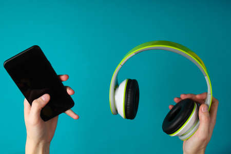 Hands hold stereo headphones and smartphone on blue background. Gadget syncの写真素材