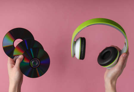 Hands hold cd discs and headphones on pink pastel background.