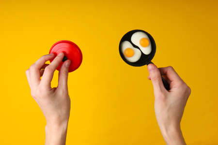 Female hands hold a mini toy frying pan with fried eggs on yellow background.の写真素材