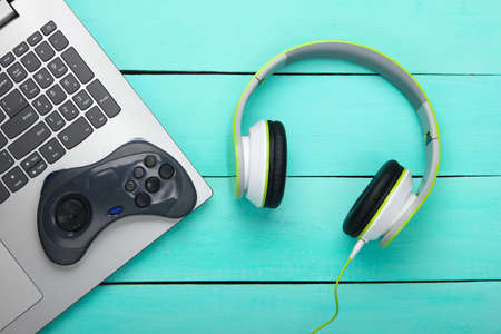 Laptop with headphones and gamepad on blue wooden background. Gaming, entertainment or leisure...