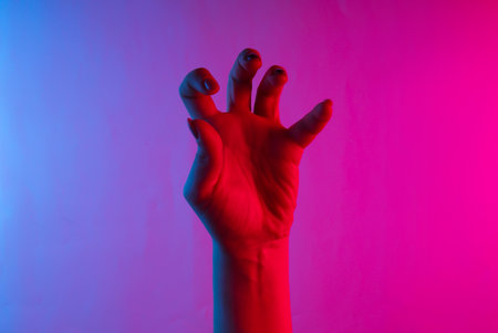 Halloween concept. Female hand with scary gestures. Neon blue-pink gradient light. Night glow. Creative artの写真素材