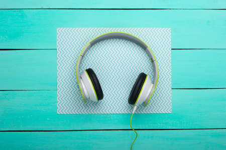 Wired stereo headphones on blue wooden boards with paper. Music lover. Gadgets. Top view.の写真素材