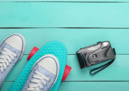 Flat lay hipster composition. Sneaker on cruiser board with camera on blue wooden background. Top...