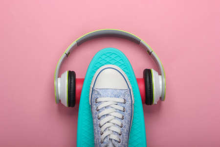 Flat lay hipster composition. Sneaker on cruiser board with stereo headphones on pink pastel background. Top viewの写真素材