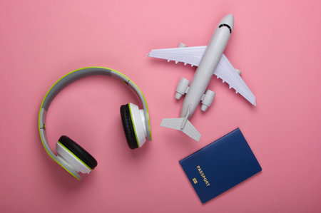 Travel concept. Headphones, airplane figurine, passport on a pink pastel background. Flight voyage, trip, journey design. Flat lay composition. Top viewの写真素材