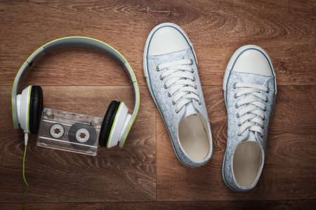 Stereo headphones, audio cassette and sneakers on a wooden floor. Retro media. Top view. Flat layの写真素材