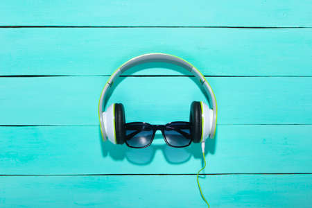 Stereo headphones with sunglasses on a blue wooden background. Top view