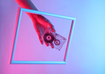 Creative art. Female hand holding audio cassette through a soaring frame with neon holographic...