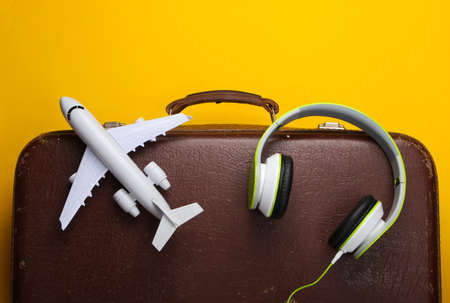 Travel concept. Old luggage, headphones and airplane figurine on yellow background. Flight voyage, trip, journey. Flat lay composition. Top viewの写真素材
