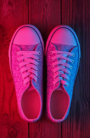Old fashioned sneakers on a wooden floor with a neon red-blue glow. Top viewの写真素材