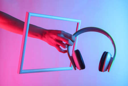 Creative art. Female hand holding headphones through a soaring frame with neon holographic light. Gradient glow.の写真素材