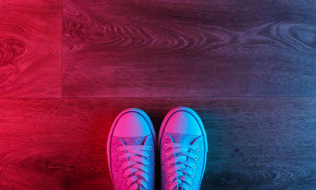 Old fashioned sneakers on a wooden floor with a neon red-blue gradient glow. Top view