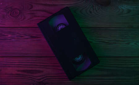 Video Cassette on wooden background. Neon purple green light. Gradient glow. Retro media and entertainment. Top viewの写真素材