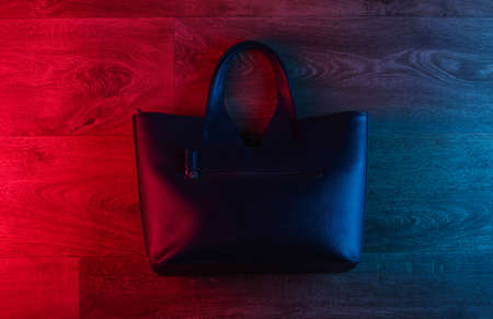 Leather bag on wooden floor with neon red-blue gradient glow. Top viewの写真素材