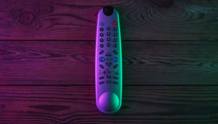 Tv remote on wooden background with green magenta neon light. Top viewの写真素材