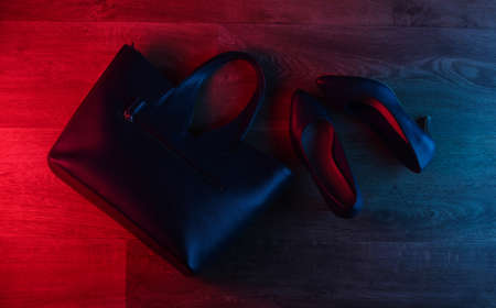 Leather high heel shoes and bag on wooden floor with neon red-blue gradient glow. Top viewの写真素材
