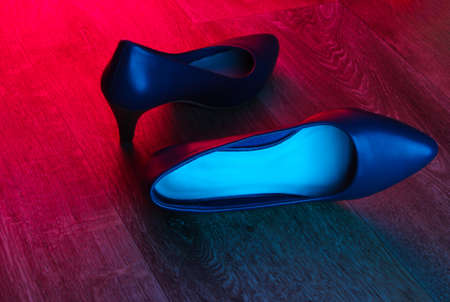 Leather high heel shoes on wooden floor with neon red-blue gradient glow.の写真素材