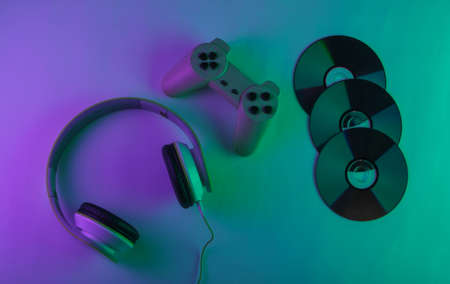 Stereo headphones with retro gamepad and cd discs. Neon purple green light. Gaming concept. Gradient glow. 80s. Top viewの写真素材