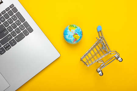 Global network, internet, online shopping, e-shop. Laptop, globe and mini shopping trolley on yellow...