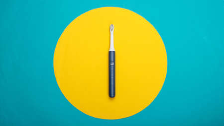 Modern electric toothbrush on blue background with yellow circle. Top view. Teeth care. Minimalism