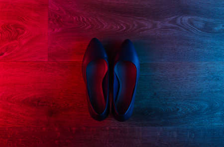 Leather high heel shoes on wooden floor with neon red-blue gradient glow. Top viewの写真素材