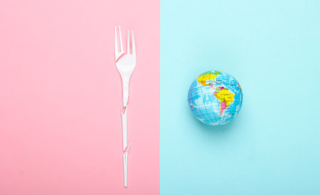 Eco still life. Save the planet concept. Plastic free. Globe and broken plastic fork on a blue-pink pastel background. Top view. Minimalismの写真素材