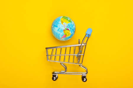 Concept of shopping and global market. Shopping trolley with a globe on yellow background. Top view