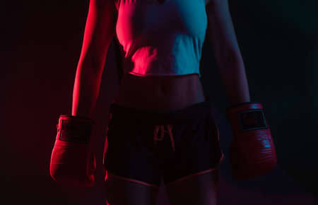 Female boxer with boxing gloves on her hands in neon blue red light on a dark background.の写真素材