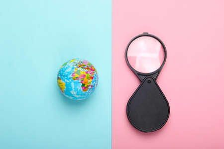 Tourism and travel concept. Globe and magnifier on a blue-pink pastel background. Top view
