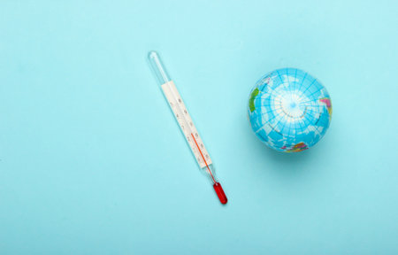 Global warming still life. Globe and thermometer on blue background. Global climate issues. Eco...