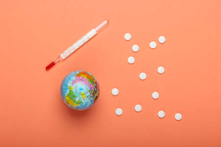 Global pandemic still life. Globe, thermometer with pills on orange background. Coronovirus outbreakの写真素材