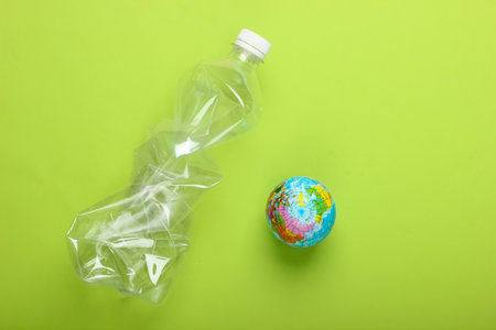 Pollution. Plastic free. Eco concept. Crumpled plastic bottle and globe on green background. Top view. Minimalismの写真素材