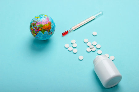 Global pandemic still life. Globe, thermometer with bottle of pills on blue background. Coronovirus outbreakの写真素材