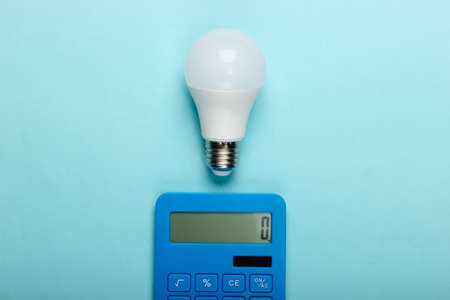 Energy saving. Calculator with led light bulb on a blue pastel background. Top viewの写真素材