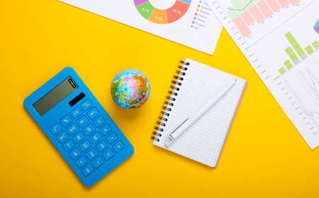 Analysis of world statistics. Globe, calculator, graphs and charts, notebook on yellow background....