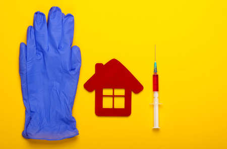 Blue latex gloves, hospital building figurineand, syringe on yellow background. Vaccination. Top viewの写真素材