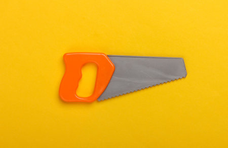 Toy mini plastic saw on a yellow background. Top viewの写真素材