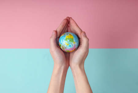 Globe in a female palms on blue pink pastel background. Planet earth care conceptの写真素材