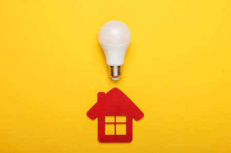 Energy saving concept. House figurine and energy-saving light bulb on yellow background. Top viewの写真素材