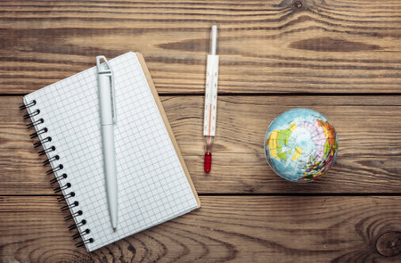 The problem of global warming. Globe, thermometer with a notebook on wooden table. Top view