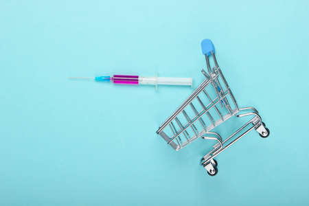 Vaccination. Supermarket trolley with syringe on a blue pastel background. Top viewの写真素材