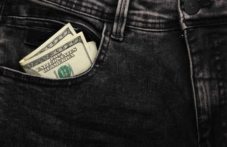Hundred dollar bills in the front pocket of black jeans close-up.