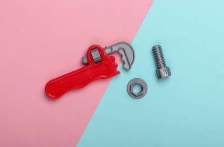 Plastic toy adjustable wrench and nut with bolt on blue-pink pastel background. Top viewの写真素材