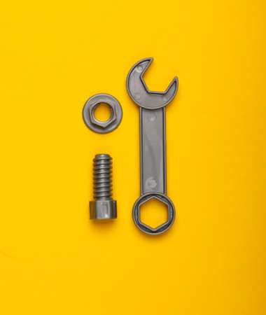 Toy wrench and nut with a bolt on yellow background. Top viewの写真素材