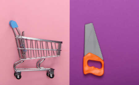 Supermarket shopping trolley with toy saw on purple pink background. Top view