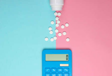 Calculation of the cost of medical expenses. Calculator and pills bottle on blue-pink pastel background. Top view. Minimalismの写真素材