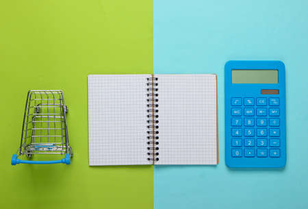 Planning and calculating shopping costs. Calculator with notepad and supermarket shopping trolley on green blue background. Top viewの写真素材