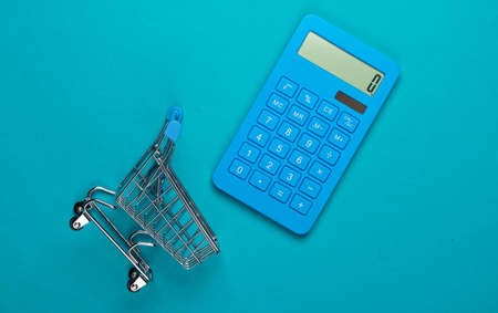 Calculation of costs for shopping, purchases in the supermarket. Calculator and shopping trolley on blue background. Top view. Minimalismの写真素材