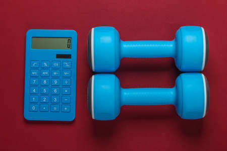 Fitness, weight loss still life. Calorie Counting. Calculator and dumbbells on red background....