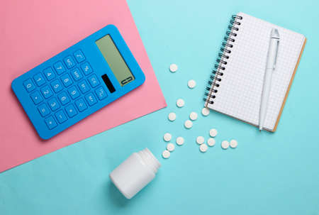 Calculation of the cost of medical expenses. Calculator, notebook and pills bottle on pink blue background. Top view. Minimalismの写真素材